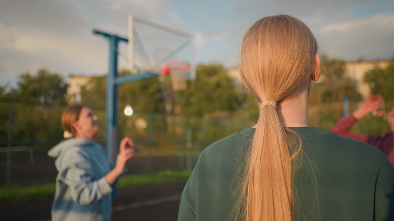 vista trasera de un atleta con suéter verde jugando al voleibol, con otro jugador con suéter azul borroso en el fondo, edificio visible en el fondo durante una sesión al aire libre soleada