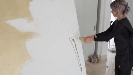 talented female artist applying paint and spreading with paintbrush on a large canvas inside her art studio - medium shot, slow motion