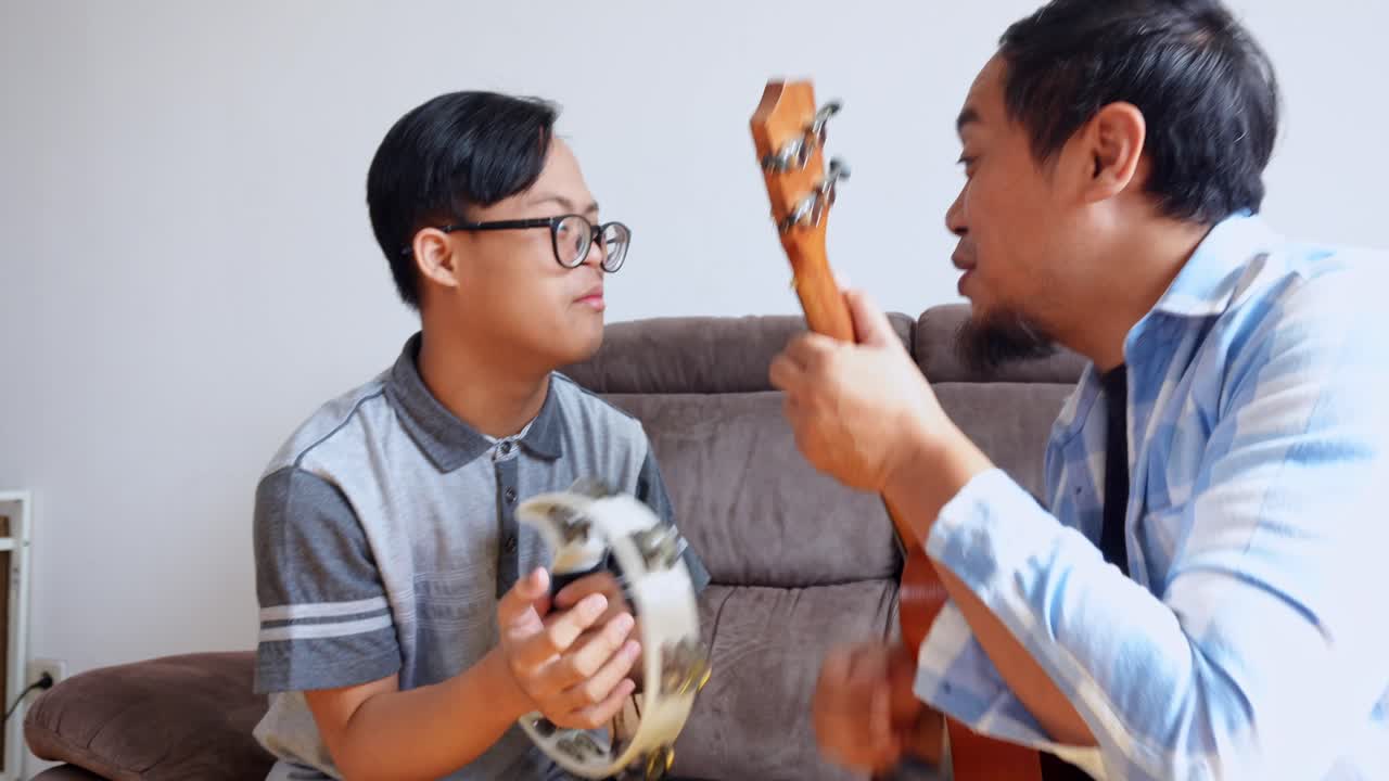 Joyful son with Down syndrome sings along to music played by father on his ukulele indoors