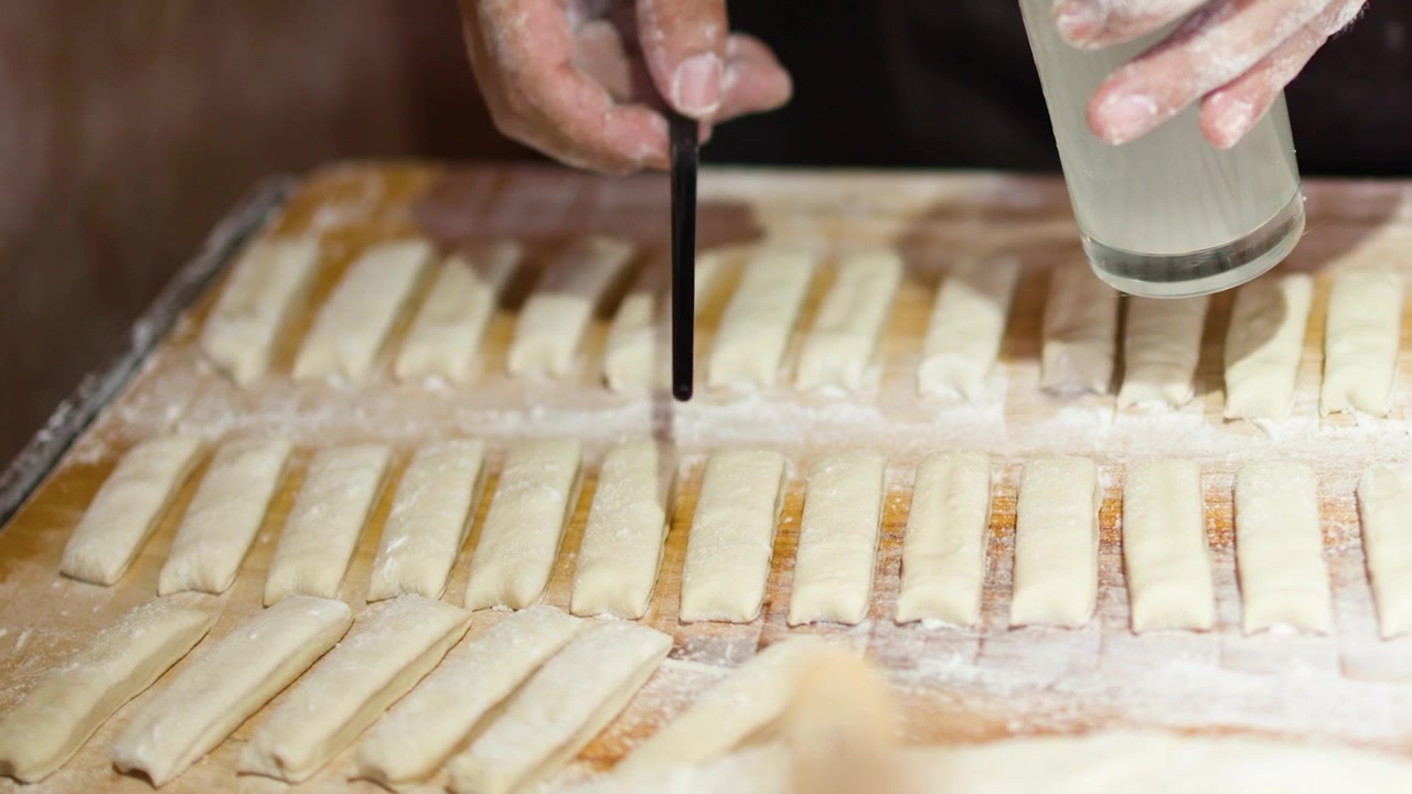 Primo piano di mani che applicano acqua a strisce di impasto per la preparazione di cibo di strada tradizionale