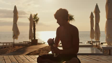 the guy takes a bottle of water and drinks on a sunny beach in the morning. relaxation and relaxation on the beach at sunrise