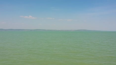 Vista-De-Drones-Hacia-Arriba-Por-La-Tarde-Desde-Las-Olas-Del-Lago-Balaton-Y-Su-Techo-De-Agua-Cerca-De-La-Orilla-De-Zamárdi,-Lago-Balaton