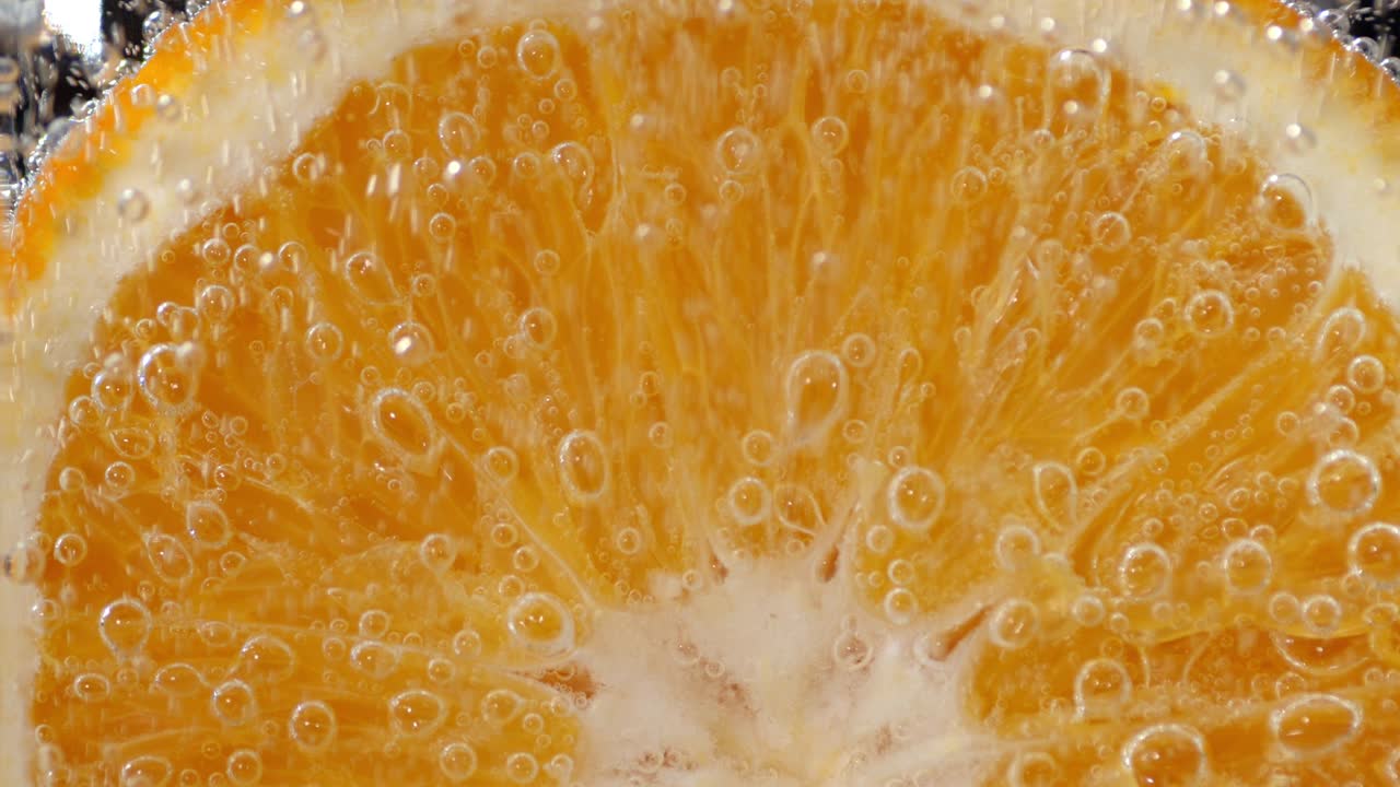 Un pezzo di arancia matura sott'acqua con bolle d'aria.