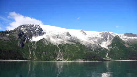 clouds roll by snow covered mountain in front of beautiful blue ocean