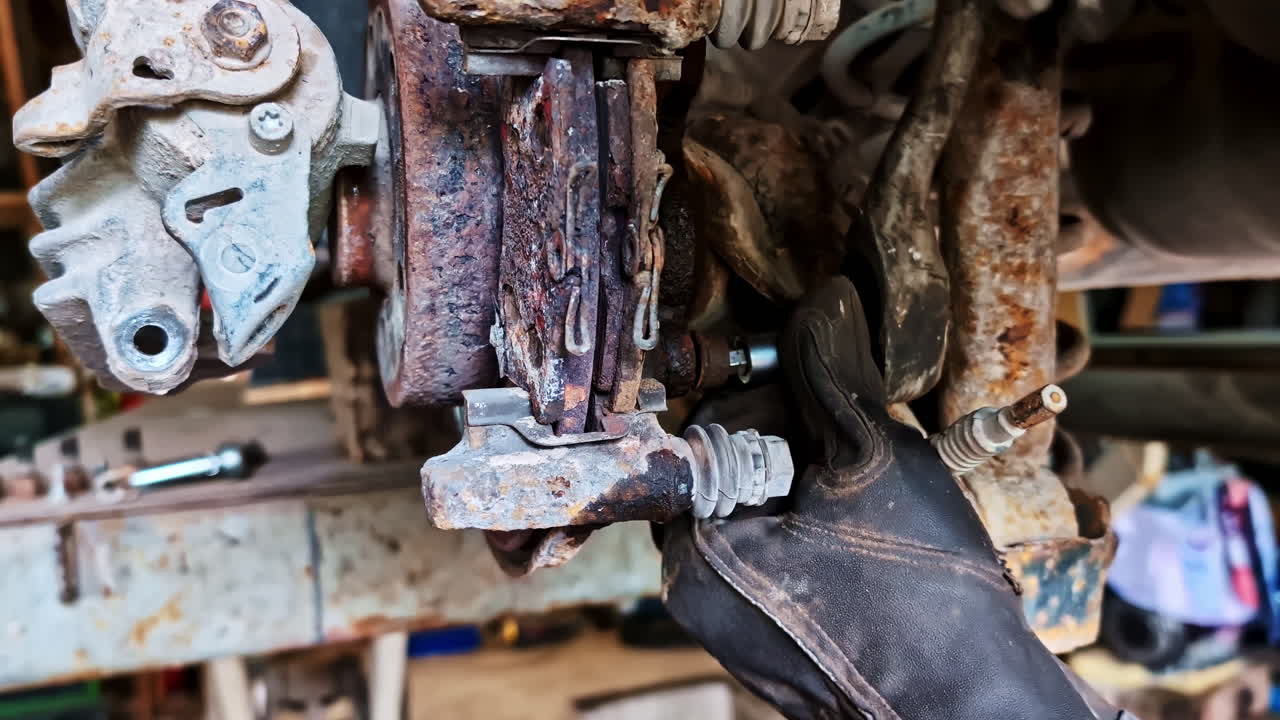 Close up of mechanic in gloves repairing heavily rusted brake caliper of car