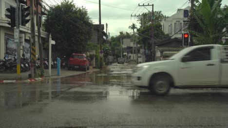 from a car stopped at red light a pick-up truck drives through a completely flooded street while scooters and cars pass in on a wet but not flooded road Flooding in Chiang Mai Thailand, September 2024