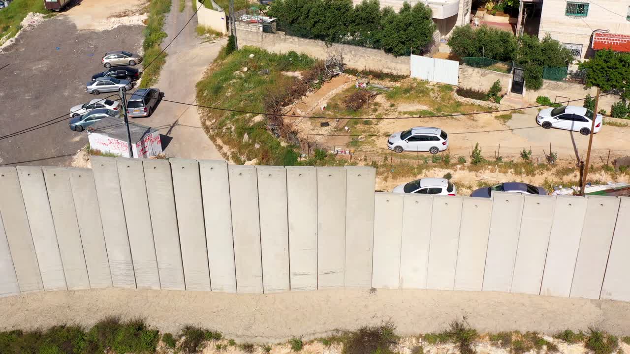 Aerial View of a Tall Concrete Separation Wall with Parked Cars and Buildings