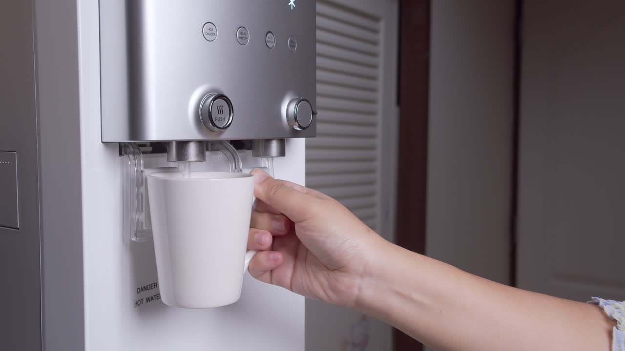 Una mujer dispensa una taza de agua caliente del purificador de agua y la vuelve a colocar.