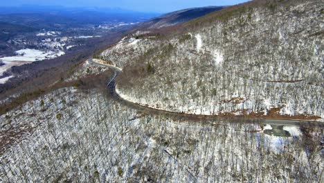 aerial drone video footage of a snowy, blue sky mountain valley road highway through the mountains in the appalachians on the shawangunk ridge, in new york state