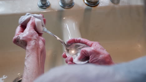 las manos arrugadas de una anciana puliendo una pieza de plata en el fregadero para quitar el deslustre y hacerla brillante