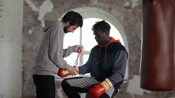 Assistant helping to put on boxing gloves to a male athlete, tie a lace