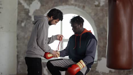 assistant helping to put on boxing gloves to a male athlete, tie a lace