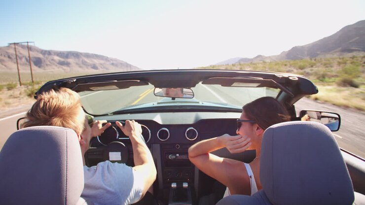 Coppia in viaggio on the road che guida un'auto decappottabile. Filmato su R3D.
