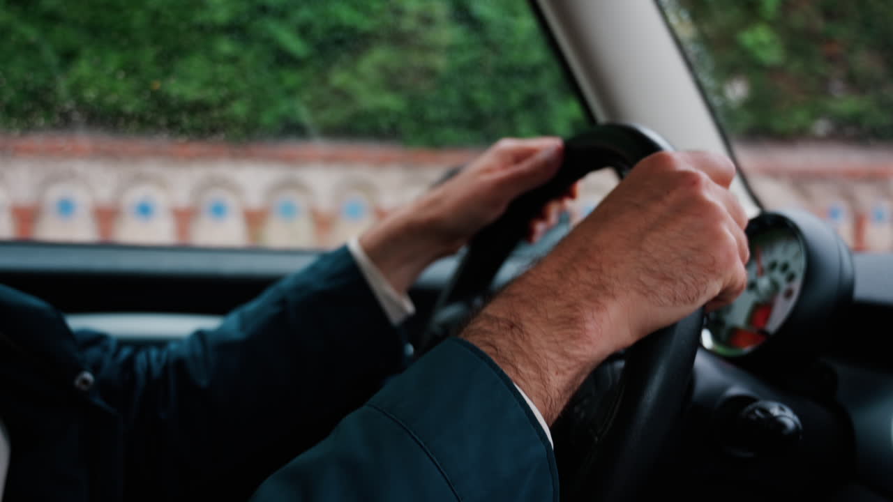 Close up of a man's hands on a steering wheel, driving a car on the road in the rain