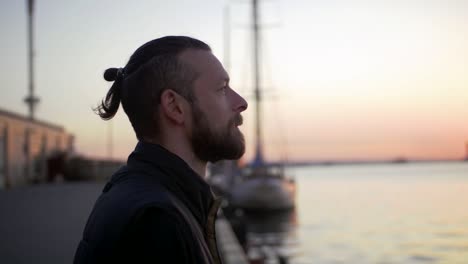 Portrait of stylish hipster man on sea port background during sunset, looking aside