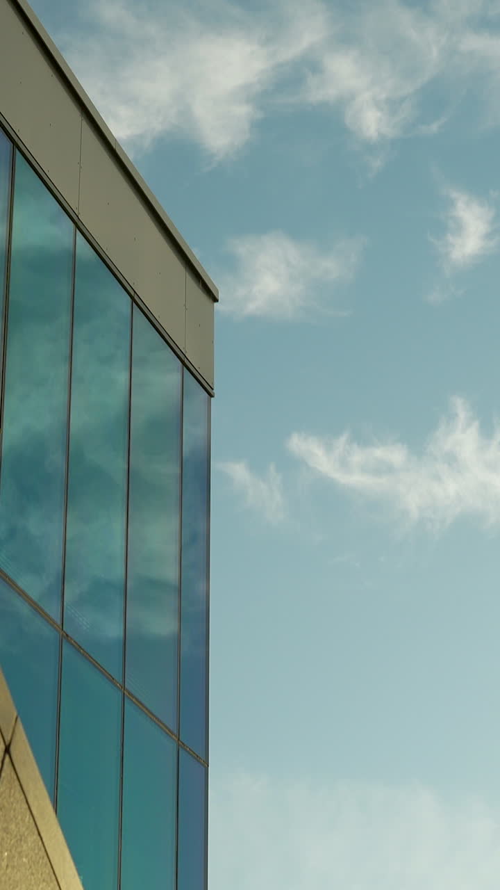 Una toma vertical de un moderno edificio de oficinas de cristal que refleja el cielo. Ideal para bienes raíces, desarrollo urbano y contenido corporativo para redes sociales