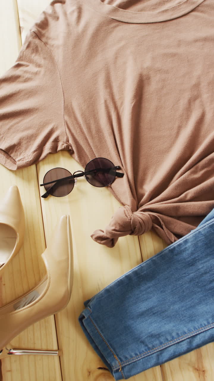Vertical video of close up of brown t-shirt, denim trousers and sunglasses with copy space