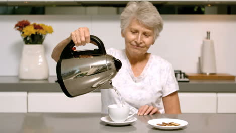 mujer anciana vertiendo agua hirviendo de la tetera en una taza en la cocina