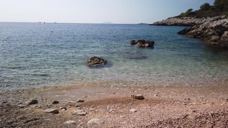 View-of-the-concrete-pier-and-pebbly-beach-of-Barjoska-Beach-on-the-island-of-Vis-in-Croatia-with-a-lone-boat-bobbing-in-the-waves