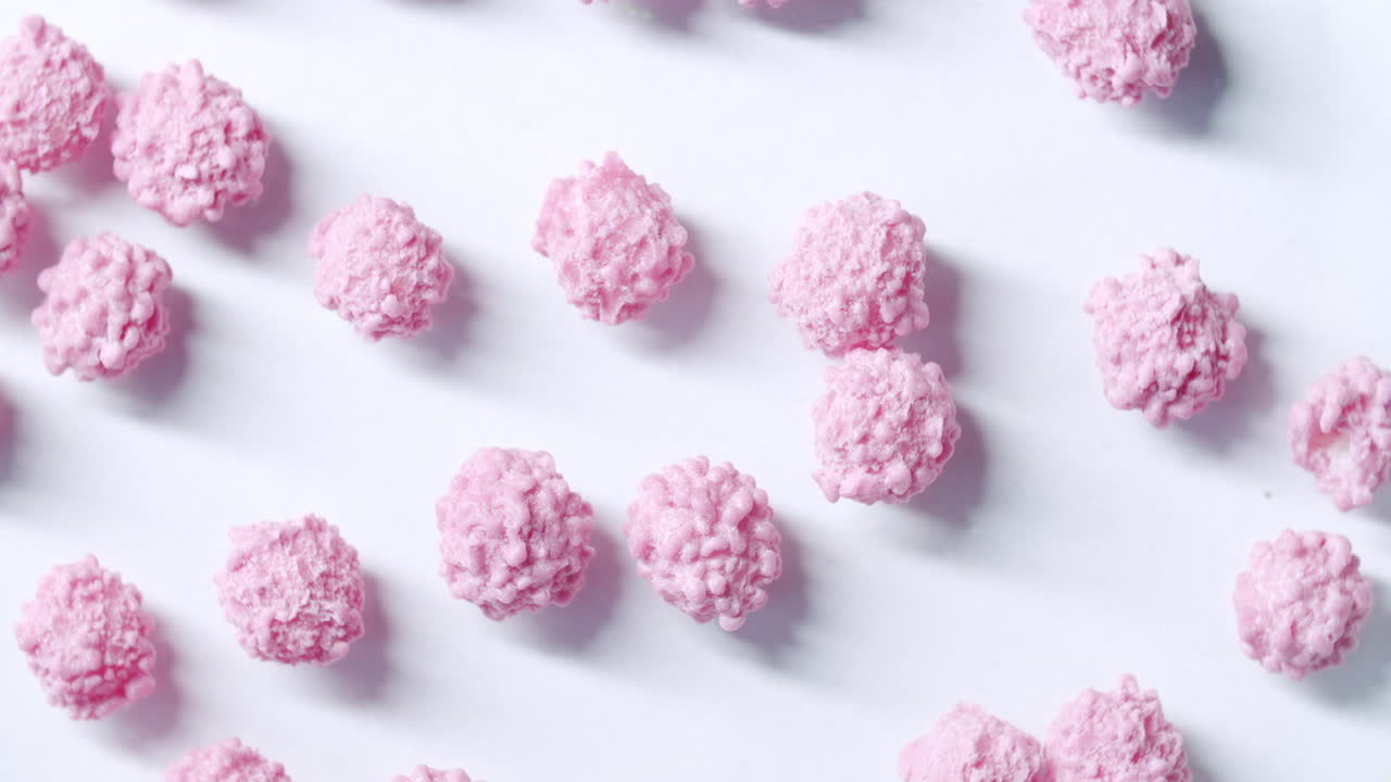 Top shot of pink particles spinning clockwise on a white surface. Commercial side light from the left. Particles looking like a virus or disease