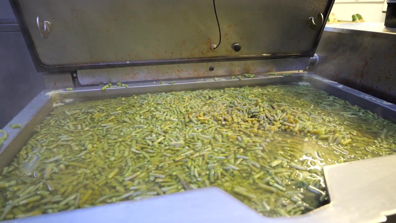 Green beans cooking in large steel pot in professional kitchen