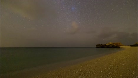 Sternenklarer-Nachthimmel-Des-Arabischen-Golfs-Wundert-Sich-An-Einem-Dunklen-Sandstrand-Im-Persischen-Meer-Mit-Felsigen-Bergen,-Szenisch-Leuchtendem-Blauem-Phytoplankton-Und-Landschaft-Des-Traditionellen-Bootssegelkonzepts-Und-Meereslebensstils