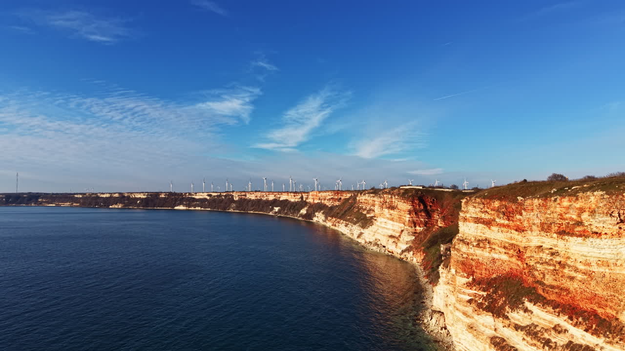 Scogliere a picco sull'acqua con turbine eoliche sullo sfondo in una giornata di sole vicino alla costa