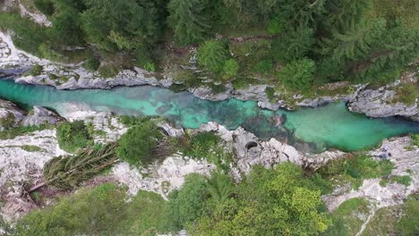 A drone speeds sideways high above a rocky gorge, looking straight down to unveil crystal-clear waters, rugged terrain, and the wider scenic wilderness of the surrounding forest