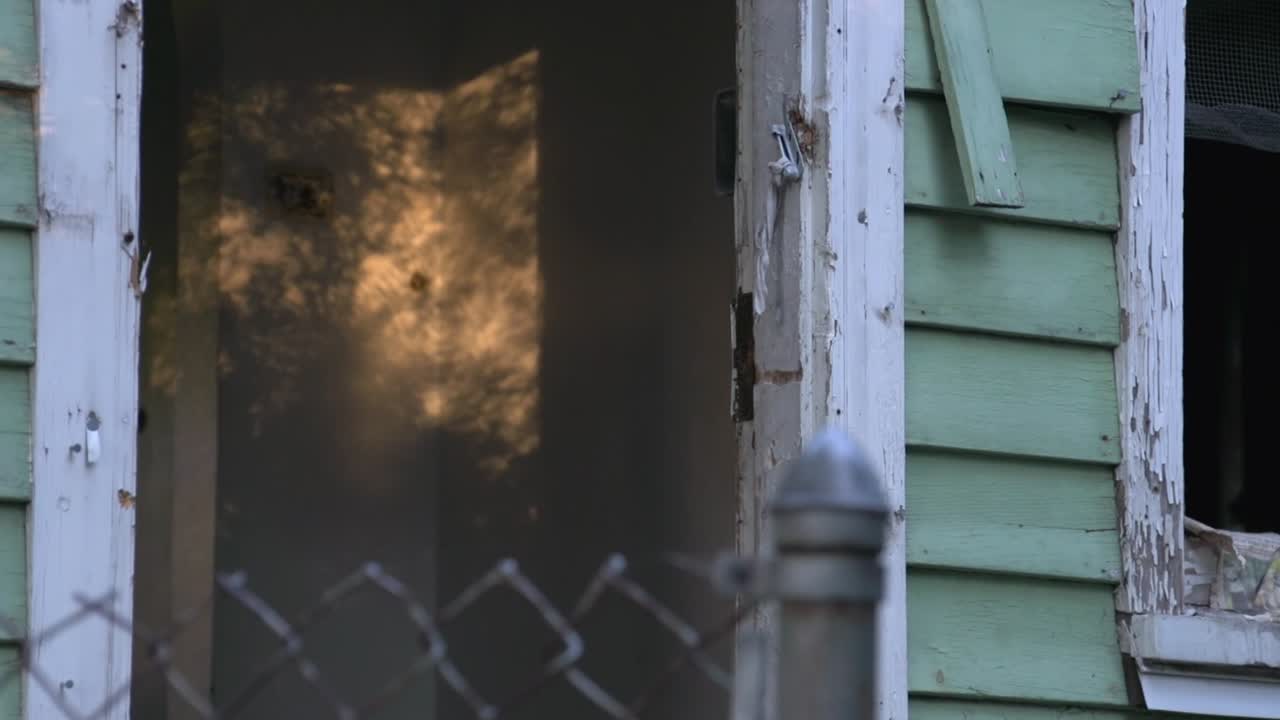 Sunlight, shadowed by the trees, shines on the light wall of a decaying, rotting-framed Detroit chalet. Shifting focus shot