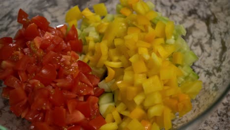 full bowl of diced sliced cut vegetables including diced tomatoes, diced bell peppers, and diced cucumber for preparing salad