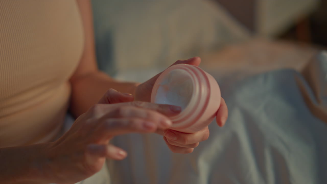 Woman hands opening cream at evening bedroom close up. Girl trying cosmetics