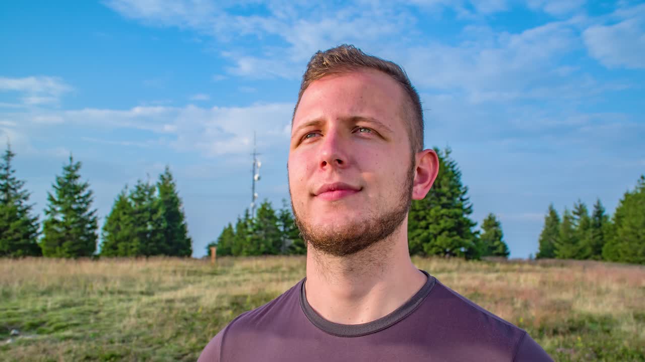 Nærbilde av en mann med et fornøyd uttrykk som står på et utsiktspunkt etter en fottur