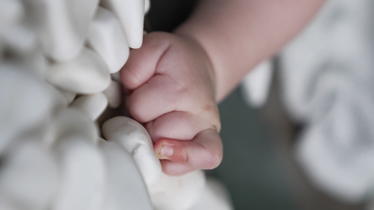 Tiny plump hand of an infant. Little hand wants to get one of pebbles scattered around. Close up. Vertical screen.