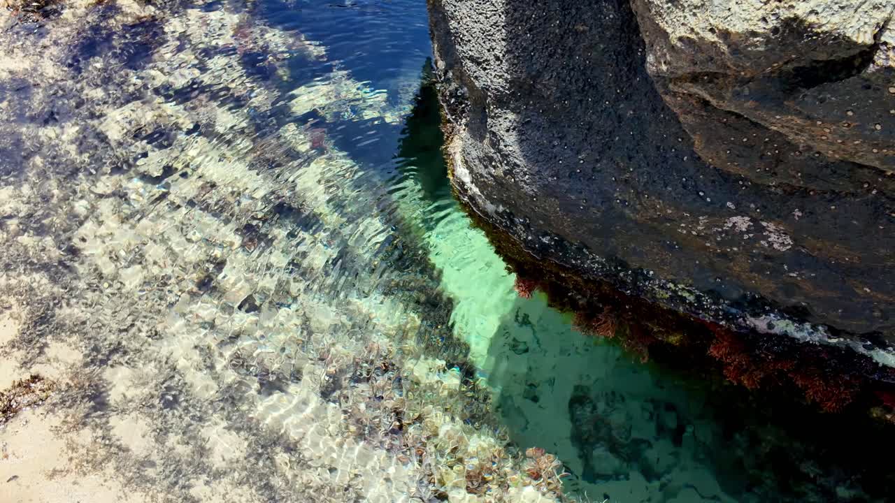 A spectacular top-down view of turquoise water meeting colorful, textured coastal rock