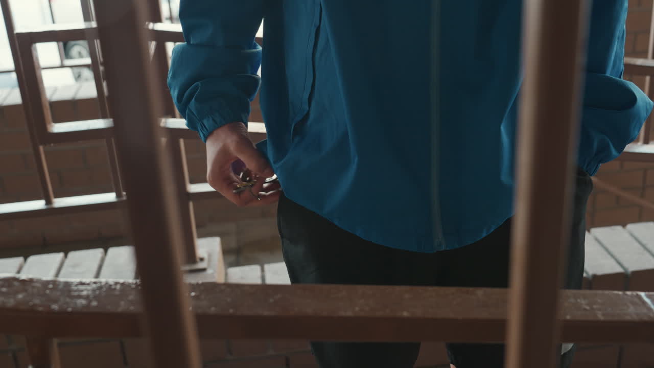 wet blue jacket hands on railing, standing on wooden balcony under light rain, droplets collecting on railing, muted city light through overcast sky, contemplative stillness, slow hand movement
