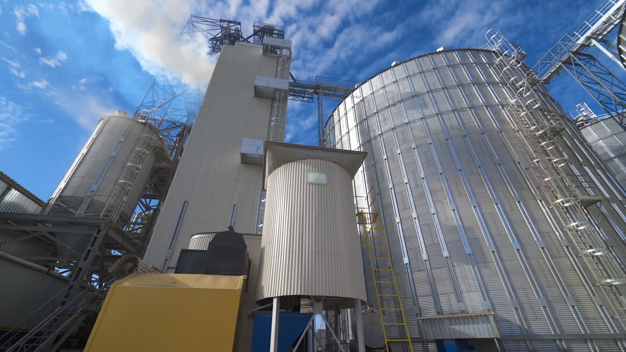 Exterior of aluminum equipment of a modern complex. Thick white smoke goes into the air from the large agricultural plant during grain processing.