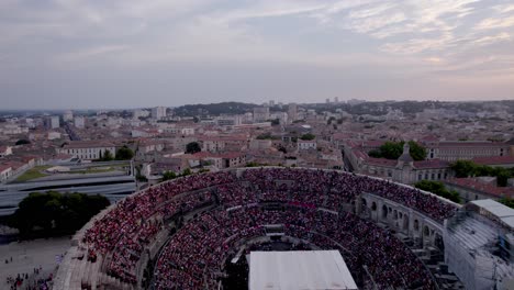 Drone-traveling-over-the-Arena-of-Nîmes-at-sunset,-people-are-waiting-for-the-stromae-concert