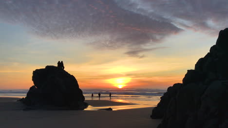 people sitting on rocks and walking on beach at sunset at the oregon coast