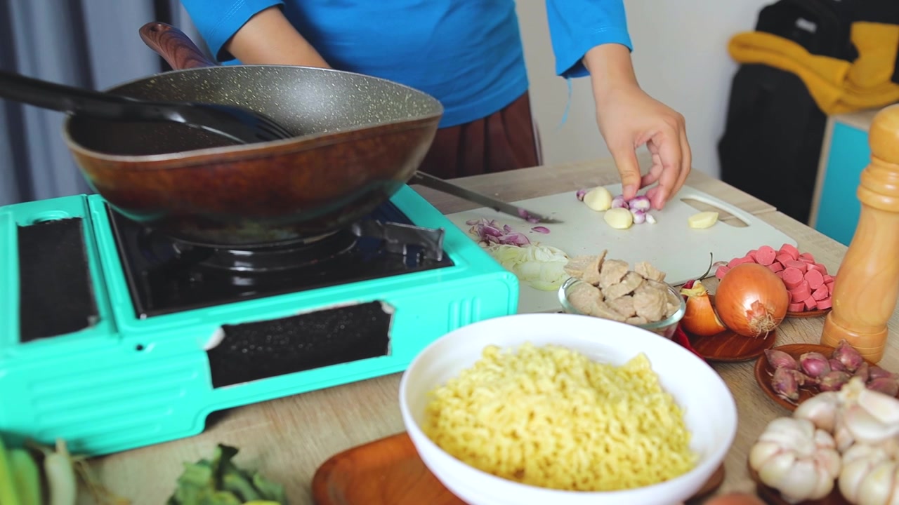 Pemandangan dapur yang menunjukkan tangan mengiris bawang merah di atas talenan.