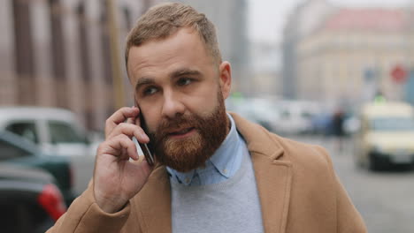 close-up view of caucasian good looking businessman with a beard walking on the street and talking on the phone