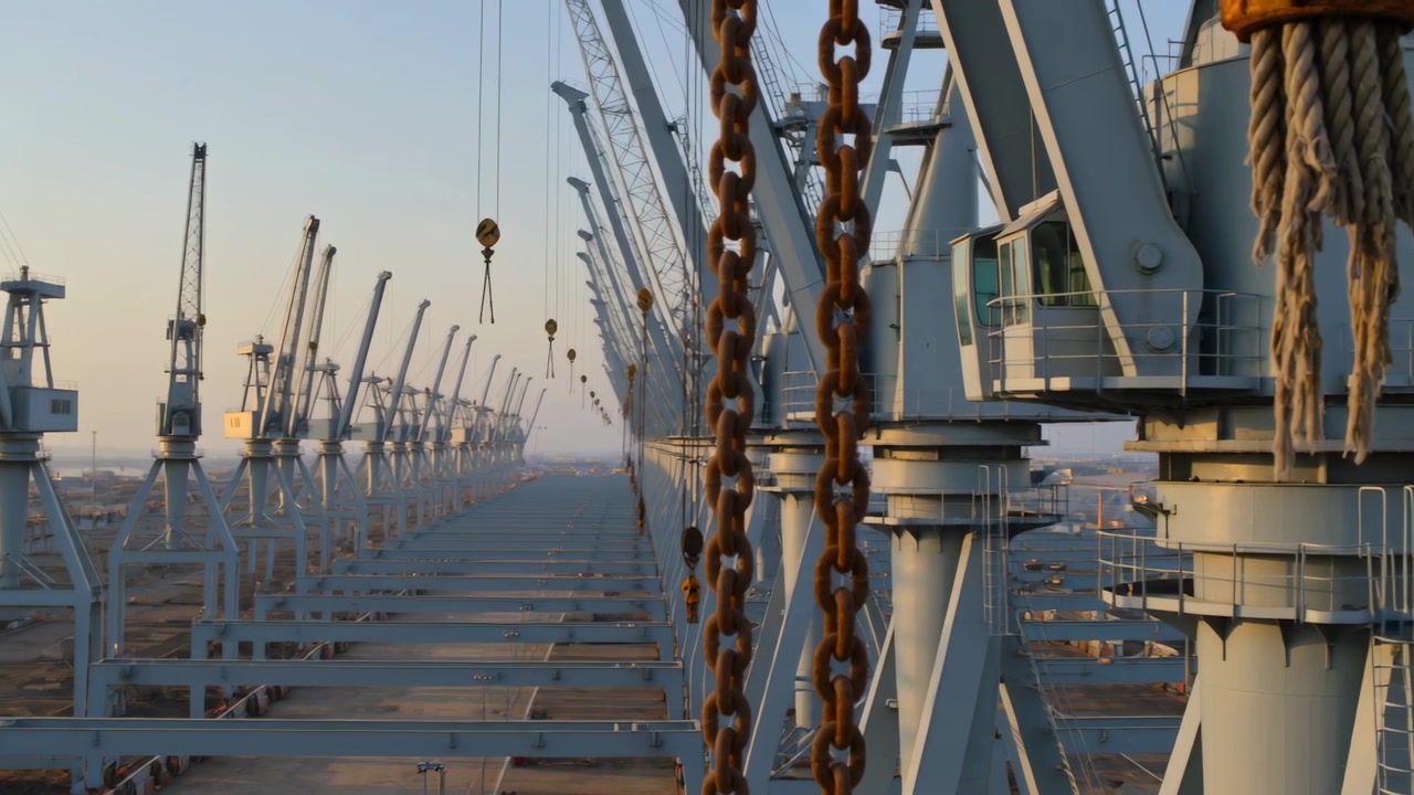 Panning camera bringing nearest gantry crane into focus at quay, to show hooks and rusted chains