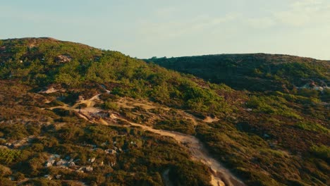 Volando-Sobre-Una-Montaña-Verde-Mientras-Una-Persona-Anda-En-Bicicleta-En-El-Corazón-De-La-Naturaleza,-Ericeira-Portugal