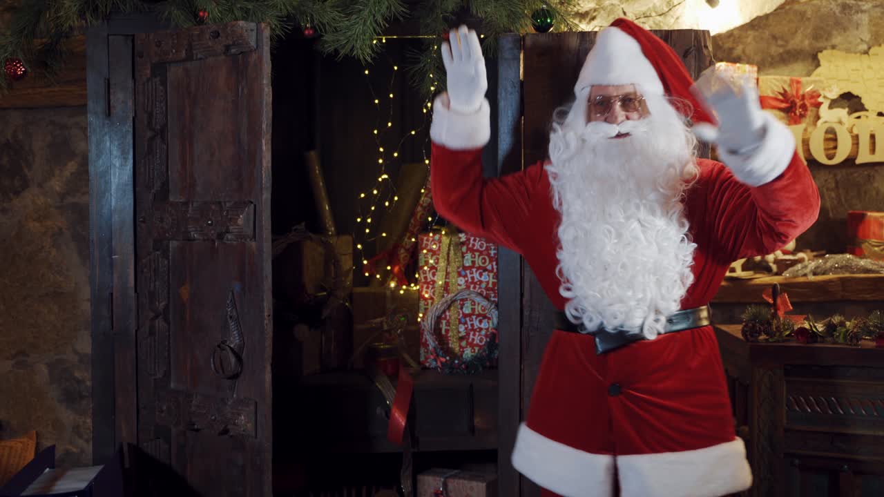 Santa Claus in red costume on Christmas background. Bearded Santa standing and moving his hands happily in his residence.