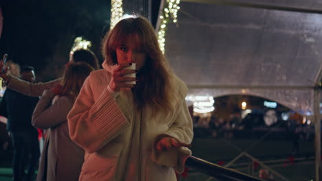 woman standing festive fairground at night sipping drink closeup. girl on fair