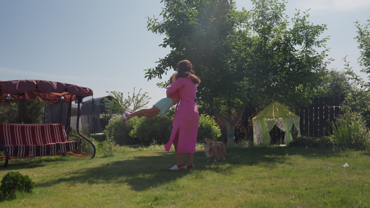 Sunny Spin Moment With Caucasian Mother Lifting Daughter Under Tree In Garden, Joyful Twirl And Laughter, Bright Afternoon, Gentle Motion, Corgi Watching Nearby, Playful Family Energy And Carefree