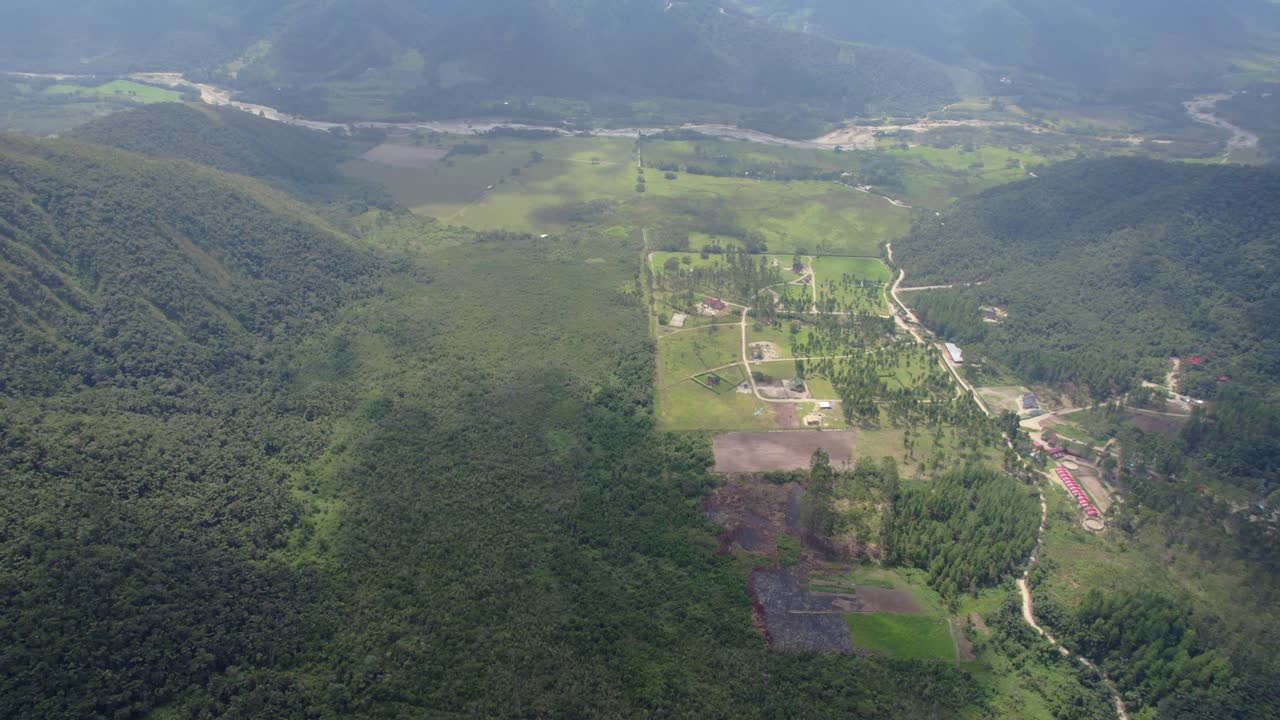 Drone zoom in aerial view of green field and hills with pine trees a cloudy day in Oxapampa, Peru.