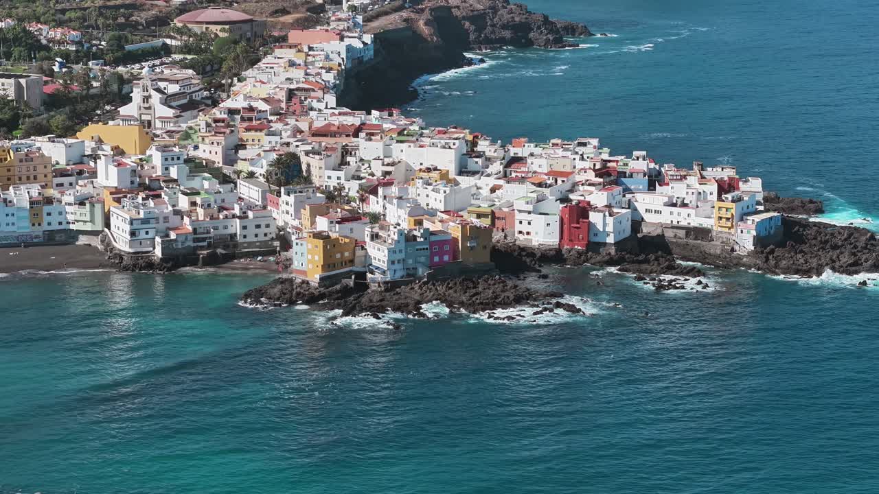 Aerial view of the colorful coastal village of Punta Brava, in Tenerife, surrounded by turquoise waves and volcanic rocks, perfect for travel, tourism, and scenic island footage