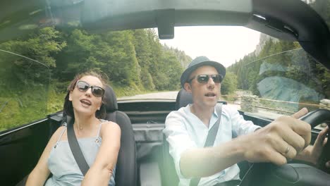 video en 4k: una pareja feliz canta las canciones mientras el coche descapotable sin techo conduce por el camino de la montaña.