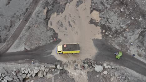 vehicles crossing a muddy stream that has flowed over a dirt road after volcanic aftermath, aerial view