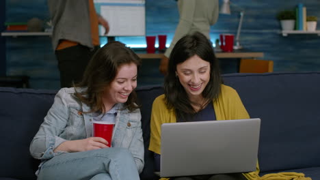 two womens sitting on couch watching comedy series on laptop computer